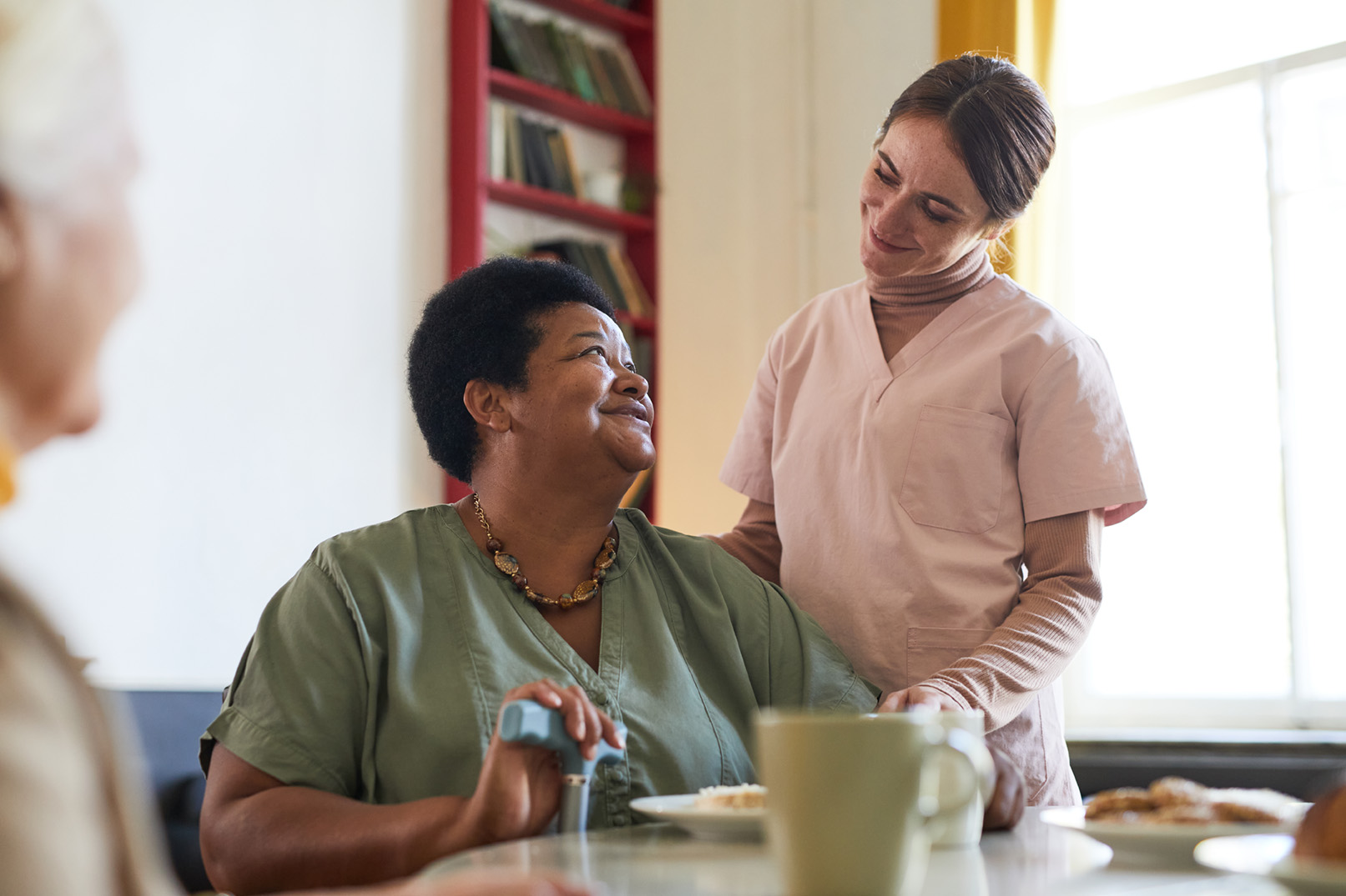 portrait-smiling-young-woman-assisting-female-patient-dinner-nursing-home-copy-space